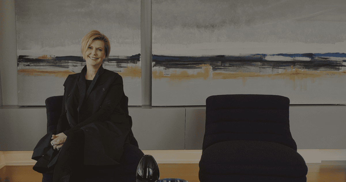A photo of a woman sitting on a cozy chair smiling at the camera. Some modern art sits behind her.