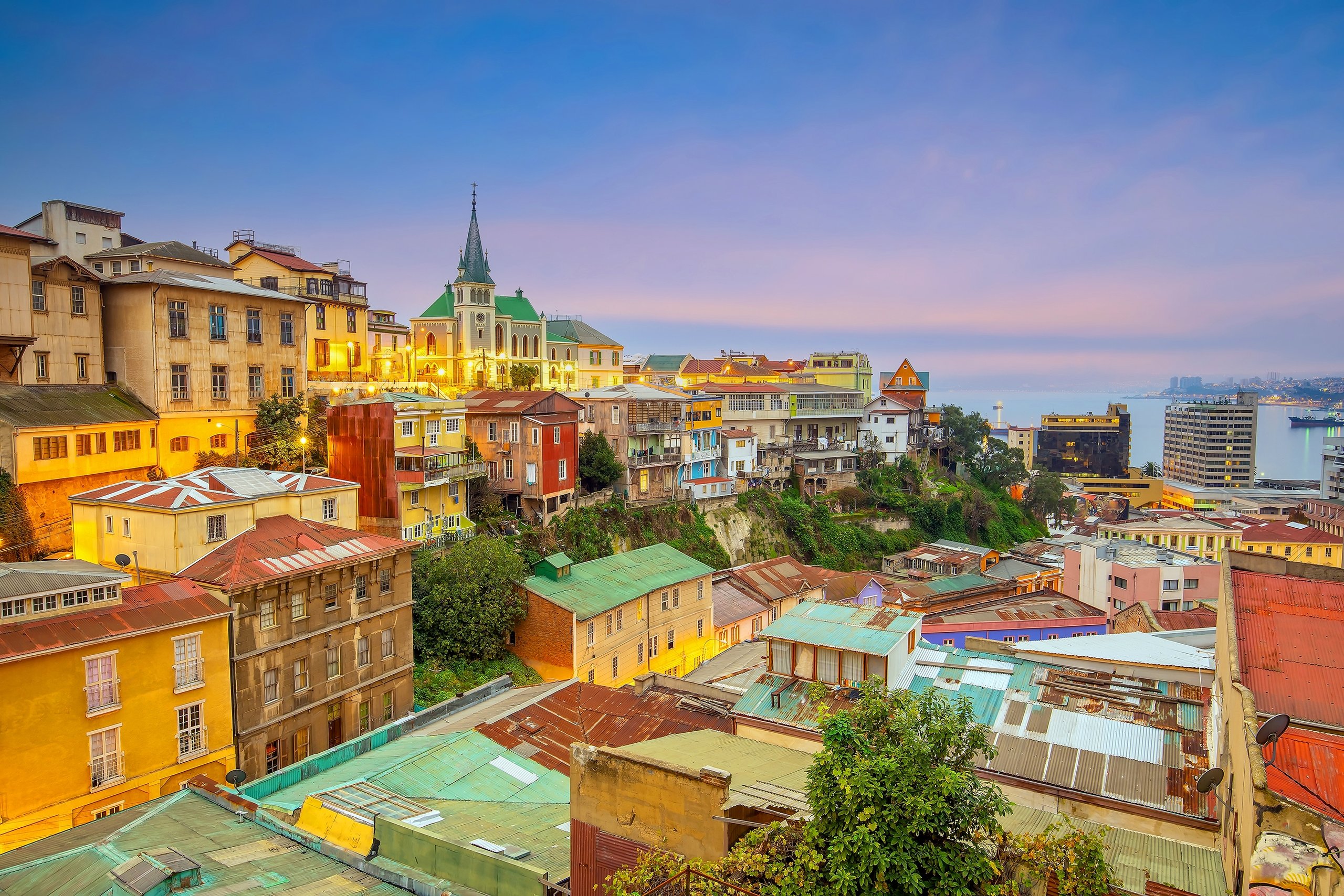 The colourful hillside houses of Valparaíso, Chile, tumbling toward the harbour beneath a church spire at dusk.
