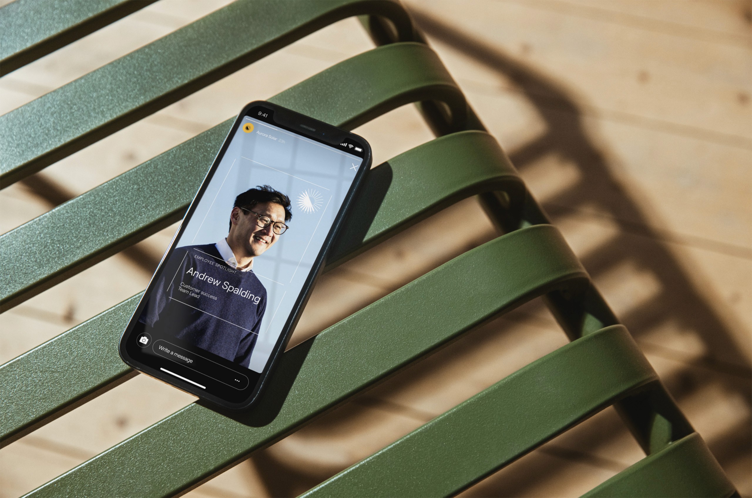 A smartphone resting on a green metal bench displays a "Employee Spotlight" screen from the Aurora Solar mobile platform. The app interface design uses warm, natural lighting and clean typography, reflecting the studio's focus on human-centered digital experiences.