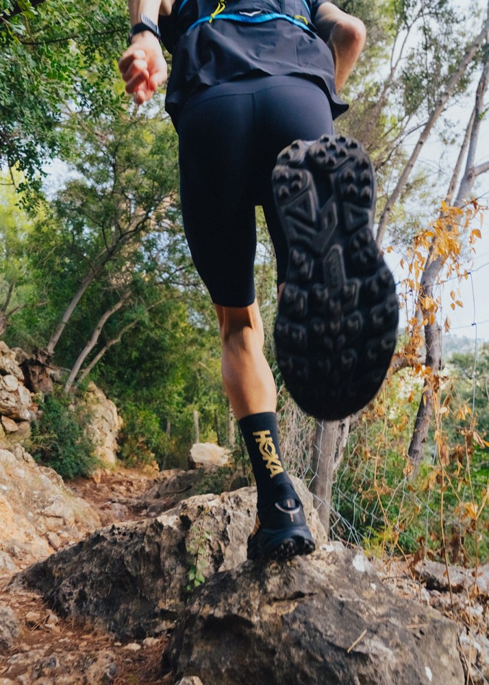 Low-angle view of a trail runner stepping over rocks, showing the HOKA Mafate 5 outsole