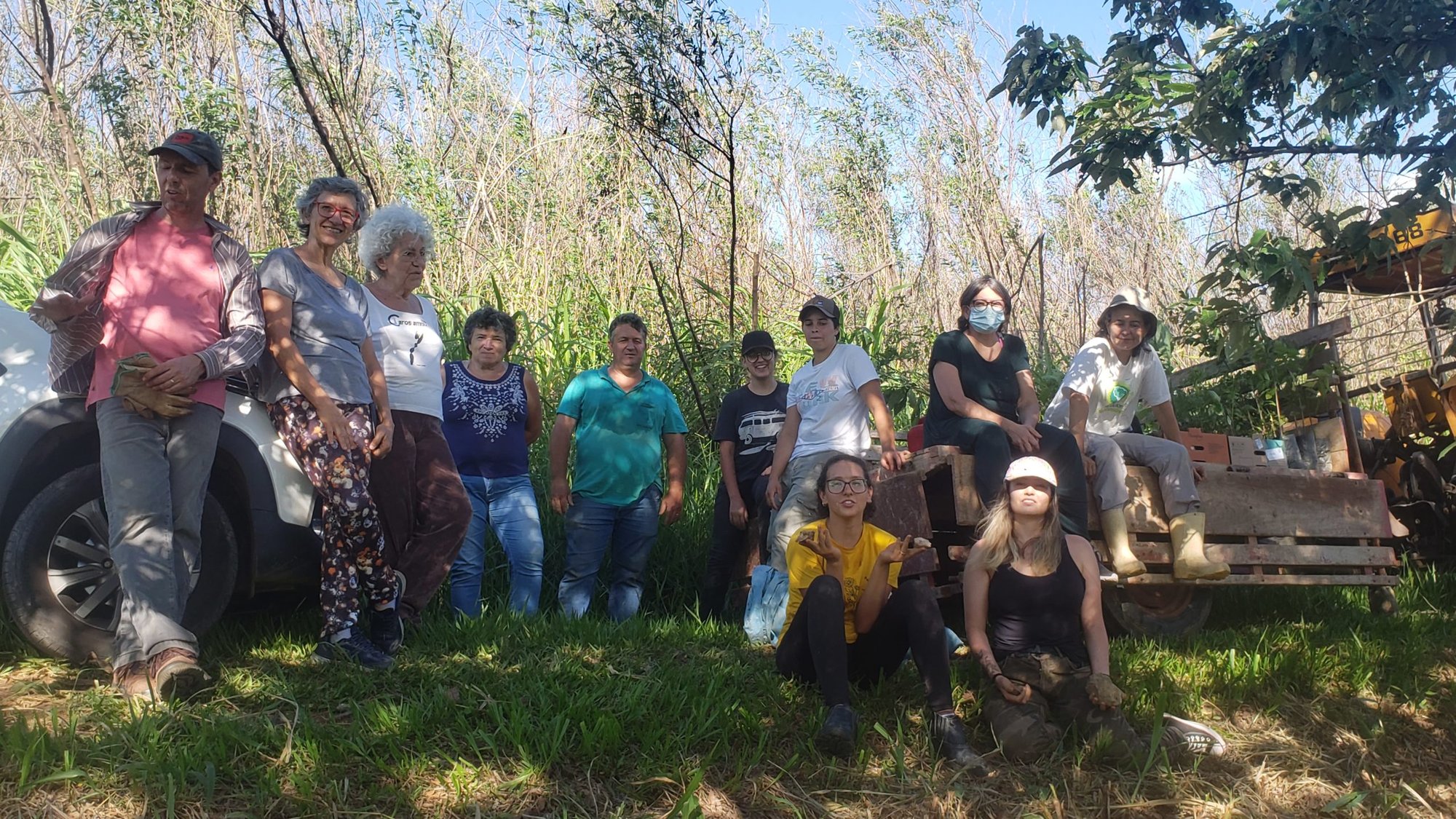 Grupo de pessoas posa sentado e em pé ao lado de picape, em campo com vegetação alta