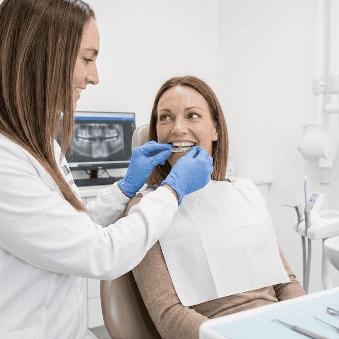 A woman receives a dental check-up while discussing her custom Invisalign aligners for optimal fit and comfort.