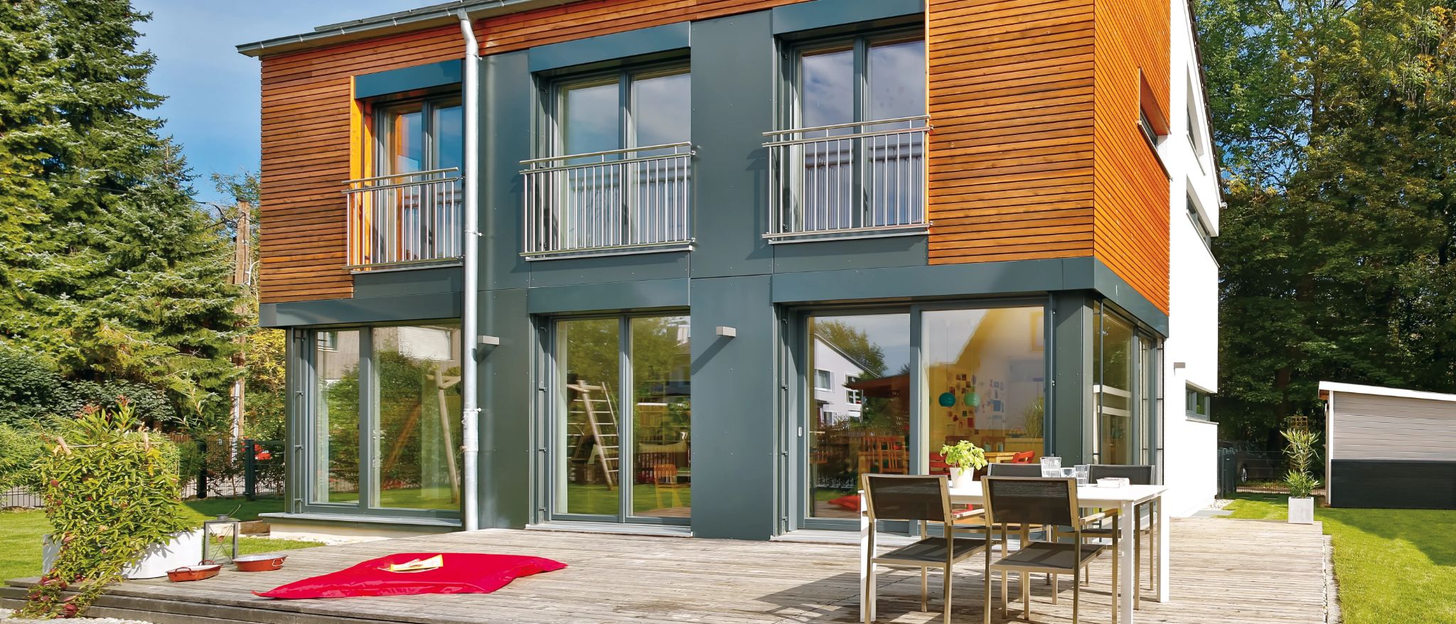 Moderne Stadtvilla mit Holzakzenten, großen Glasflächen, einer Holzterrasse und einem Garten.