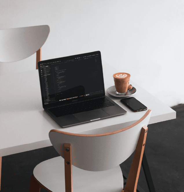 Laptop on a desk displaying a code editor next to a cappuccino