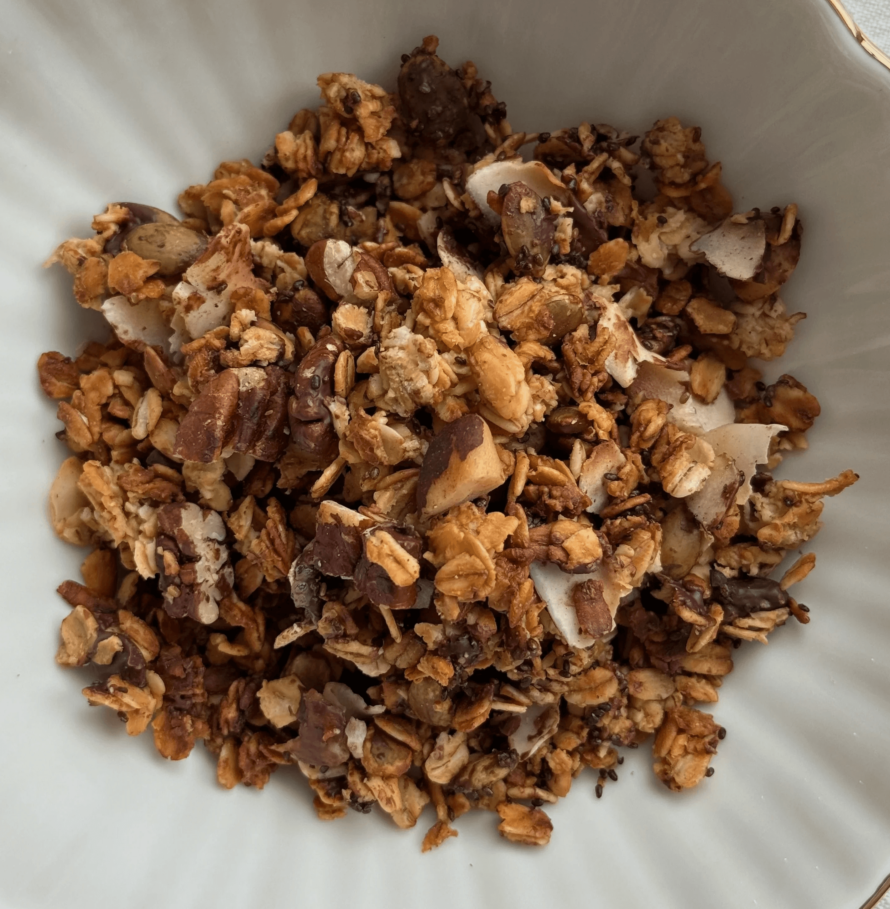 Homemade granola with nuts, seeds, and coconut flakes in a white bowl