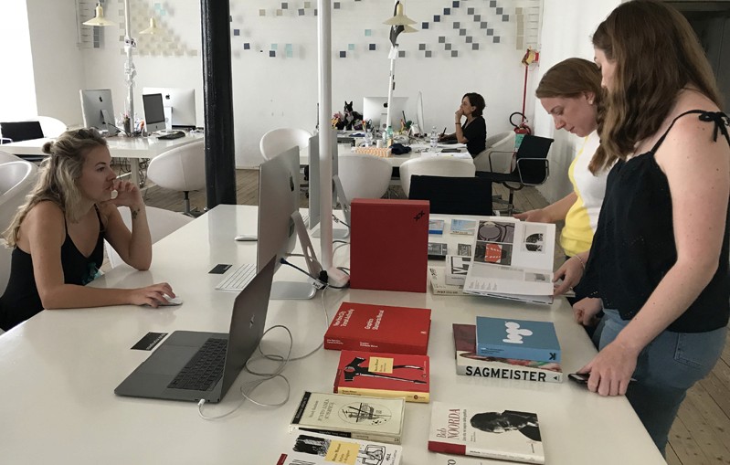 A photo of a group of students checking some bock and also looking at a pc.