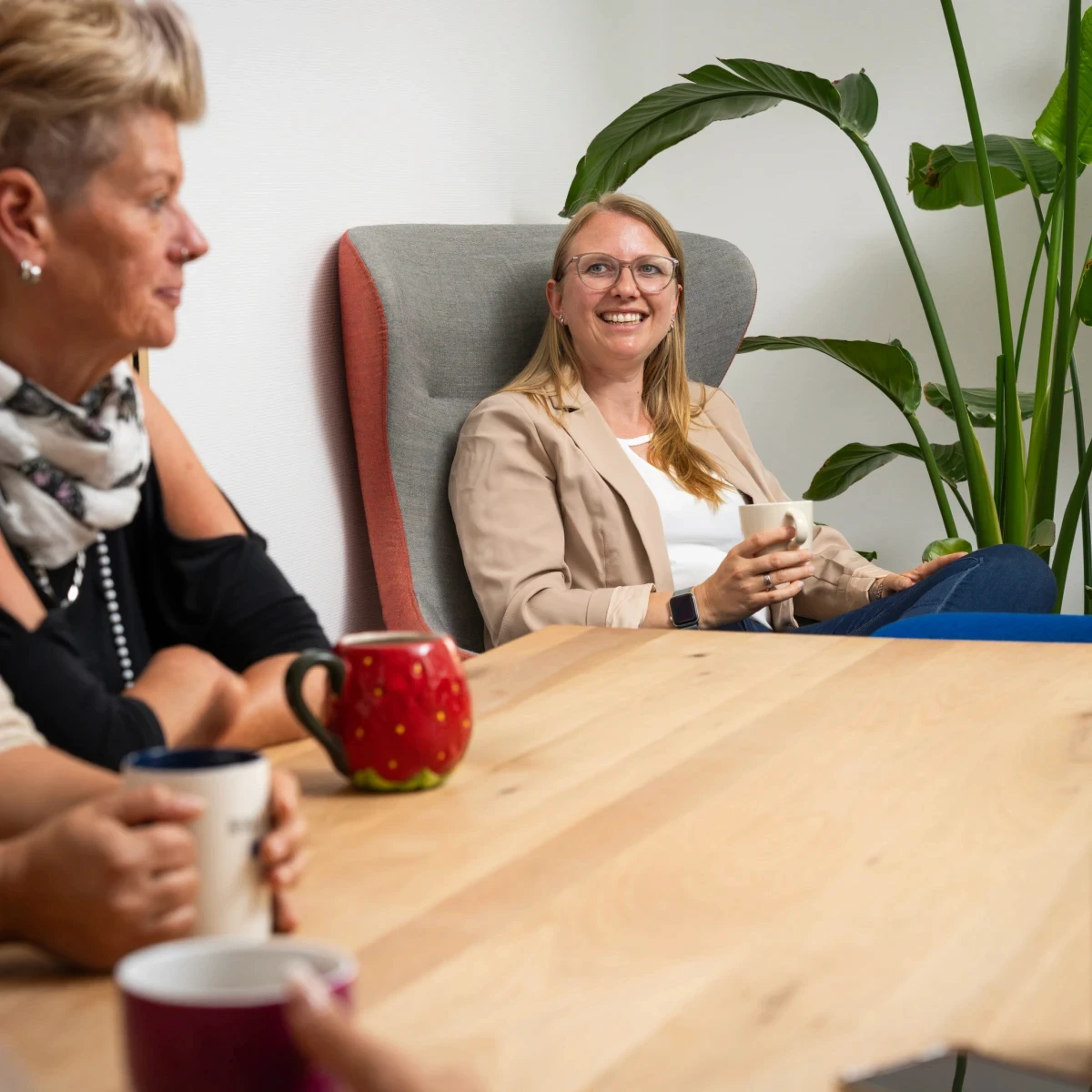 GJP-Mitarbeiterin sitzt mit einer Tasse in einem Besprechungsbereich zwischen großen Zimmerpflanzen