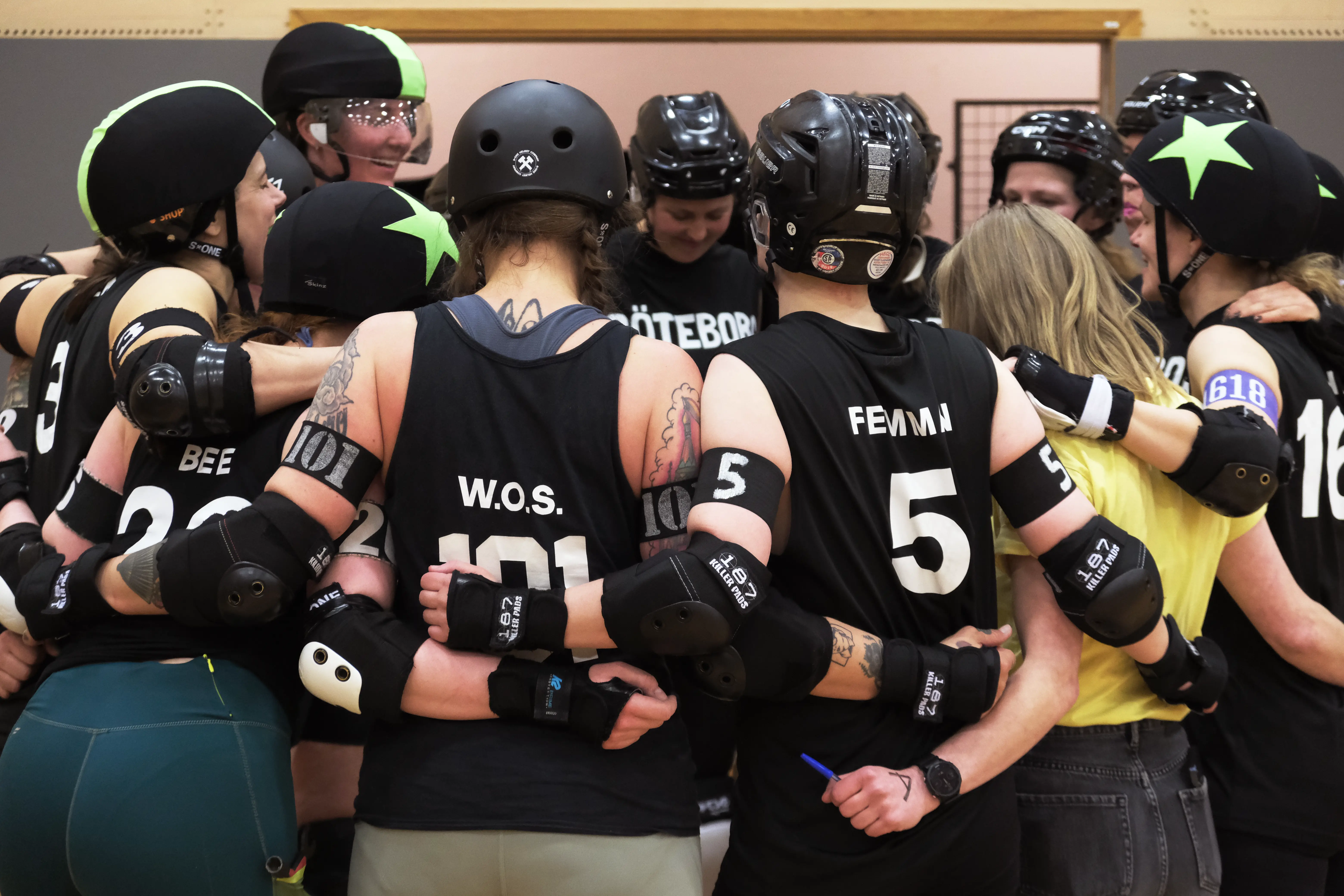 A group of Roller Derby Players in a circle holding each others backs.