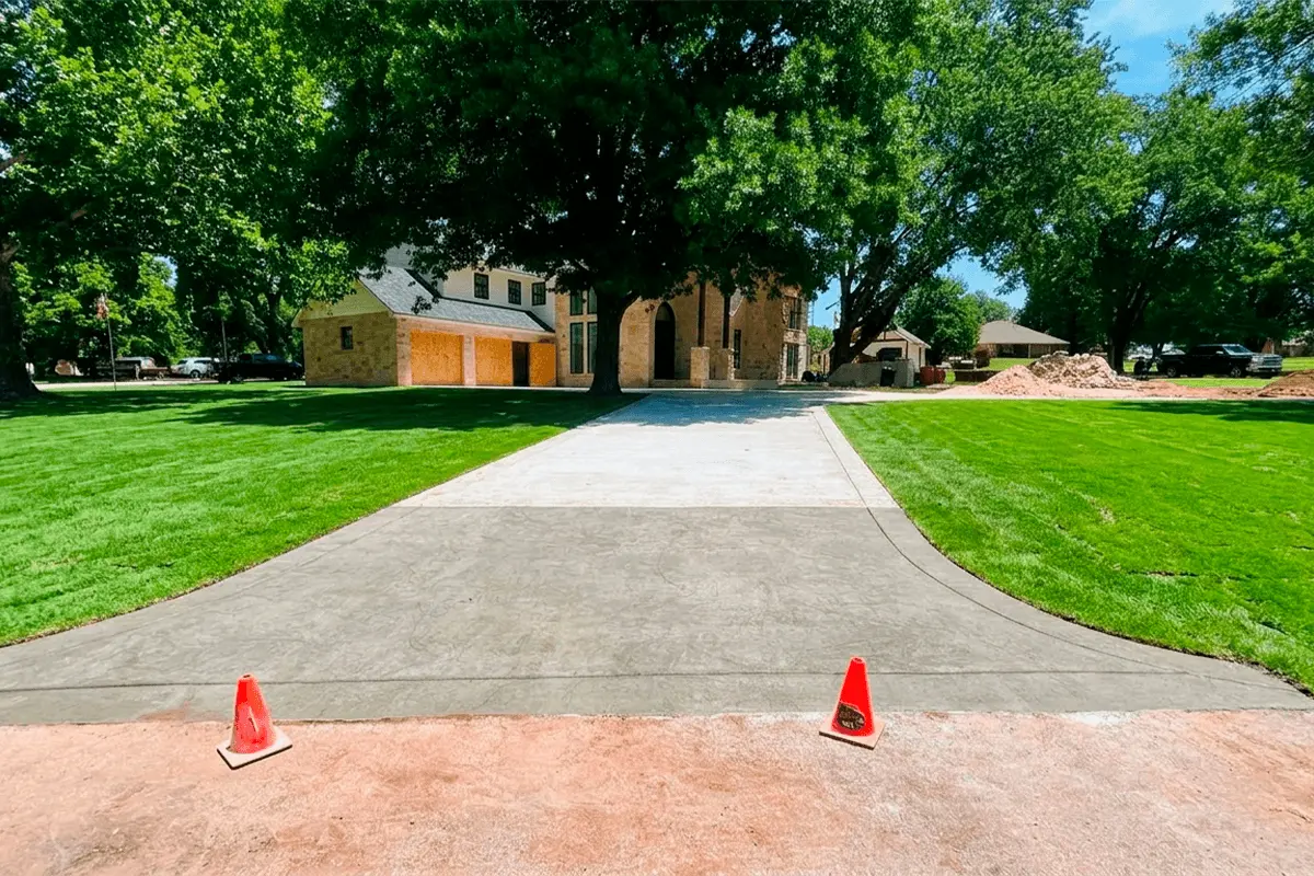 Newly constructed concrete driveway in front of a house with a lawn and trees.
