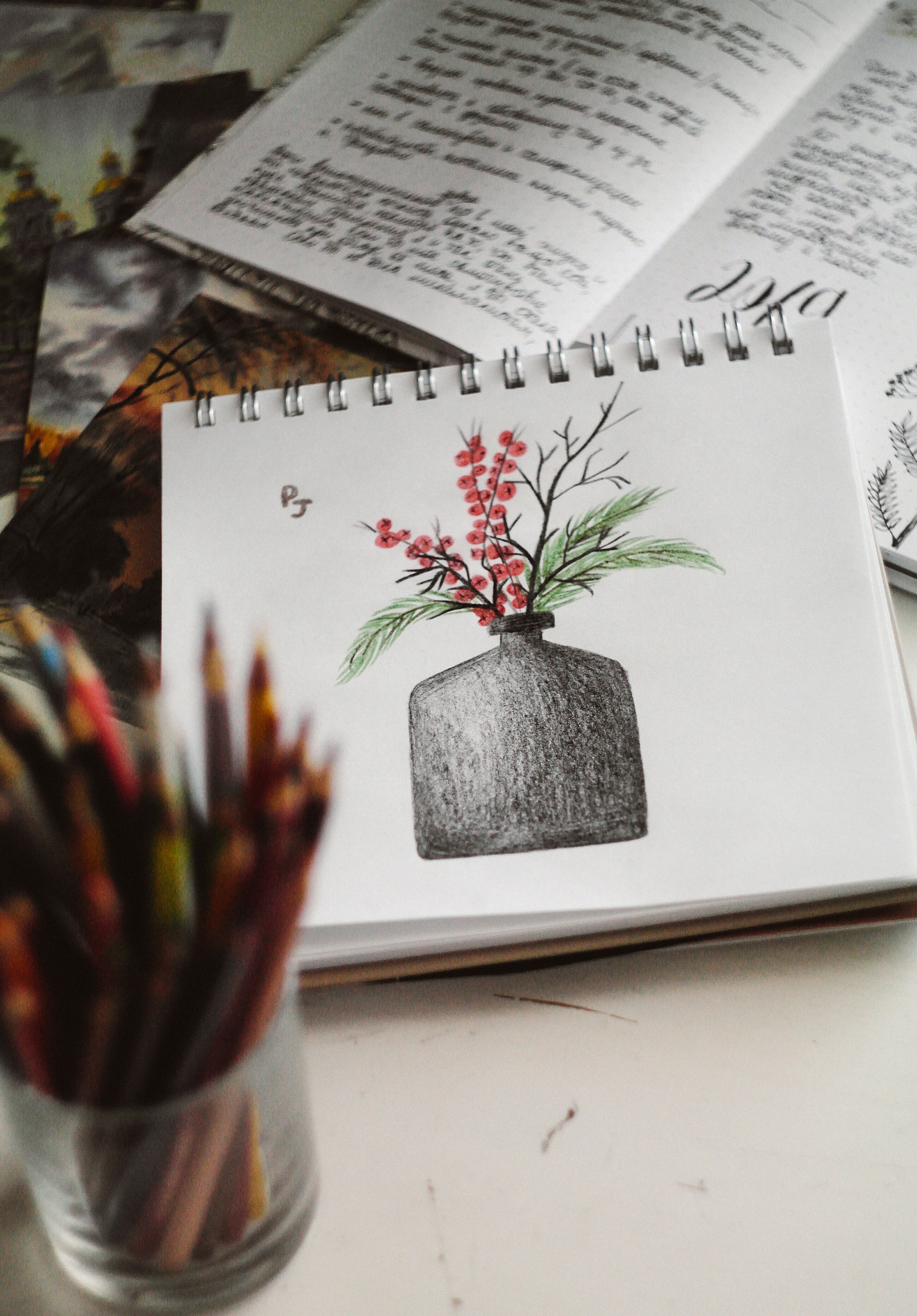 Pencil still life of a vase with red berries in a spiral sketchbook
