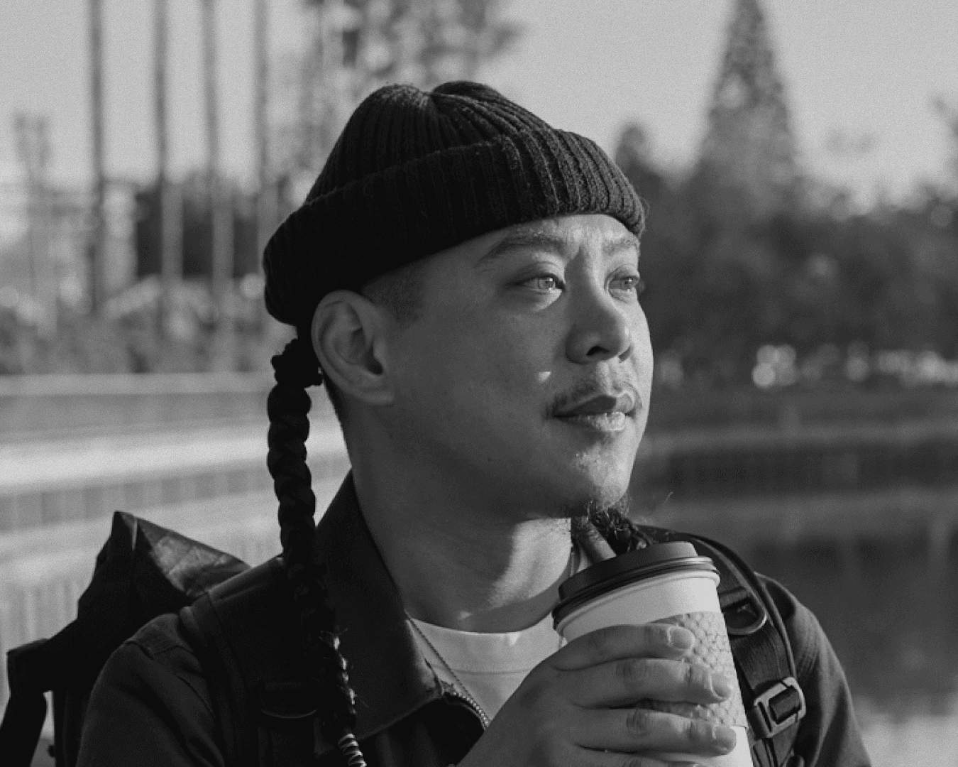 Asian man in a beanie with braids looking into the distance