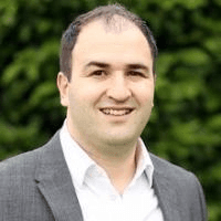 Smiling man in a grey suit jacket outdoors headshot