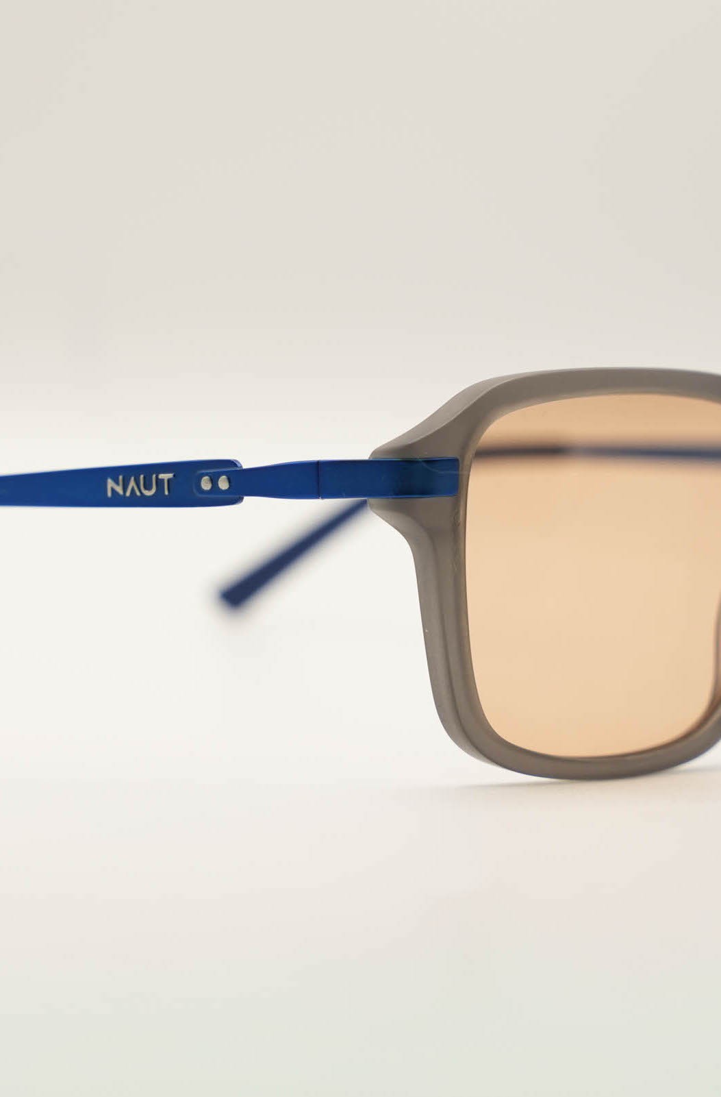 Smiling man in a white hoodie and black pants standing confidently on a bright green football field with empty stadium seats behind.