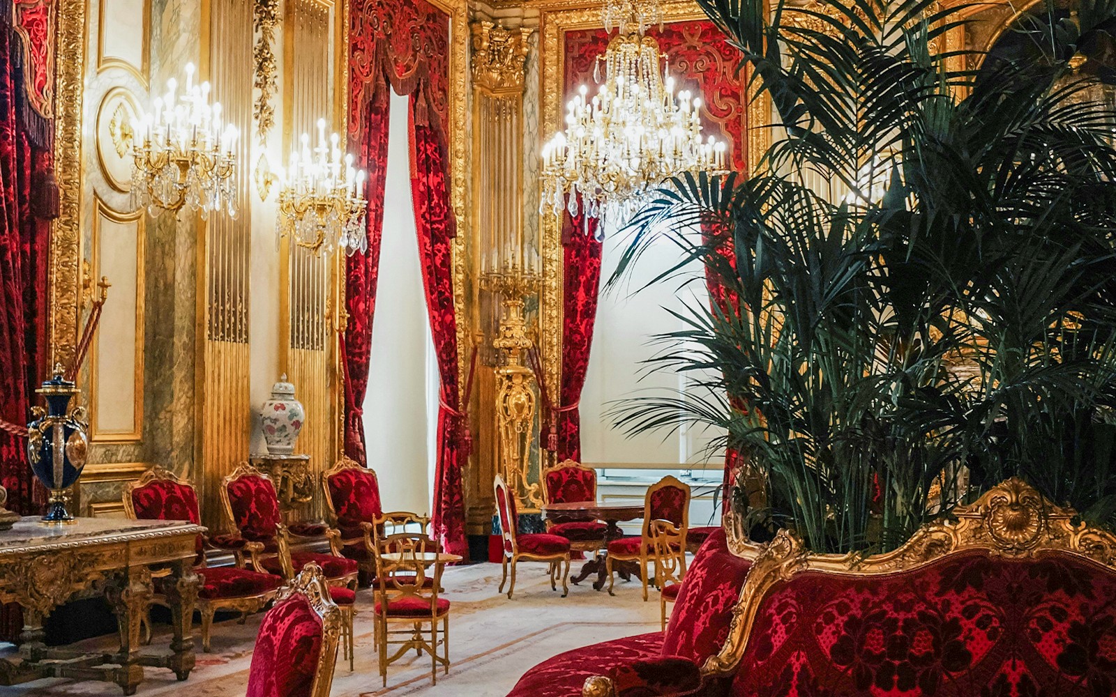 Værelse i Versailles-paladset med udsmykkede lysekroner, røde fløjlsstole og gyldent dekoration.