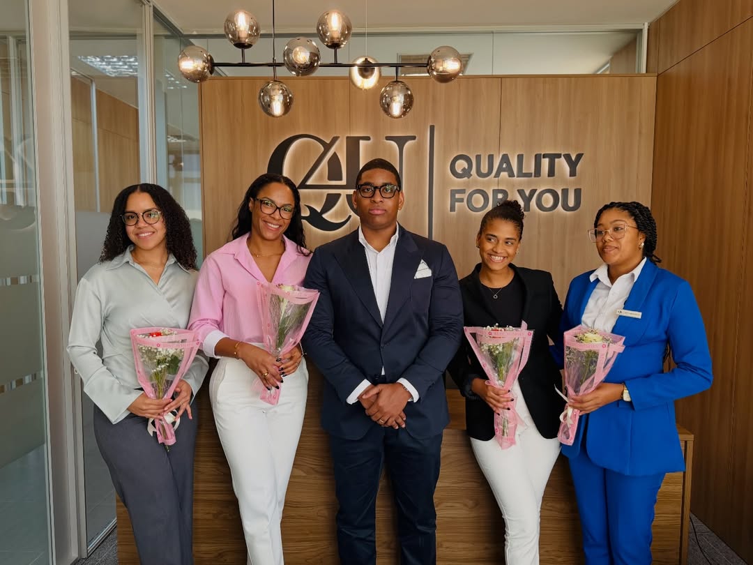 Three workers in safety gear and helmets are suspended by ropes, cleaning a modern building's slanted roof, against a clear blue sky.