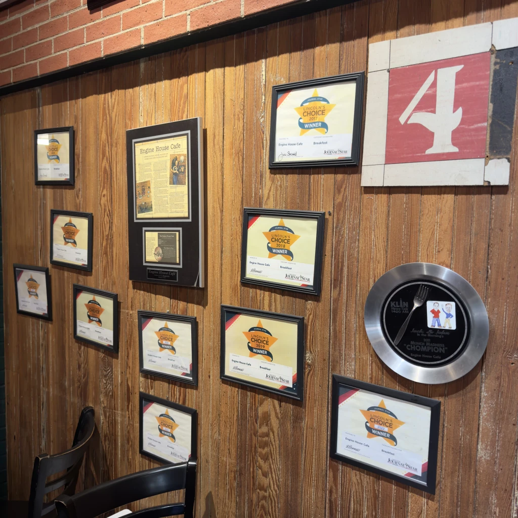 Engine House Cafe interior wall displaying framed awards, fire station memorabilia, and a sign reading ‘4’ from the original firehouse.