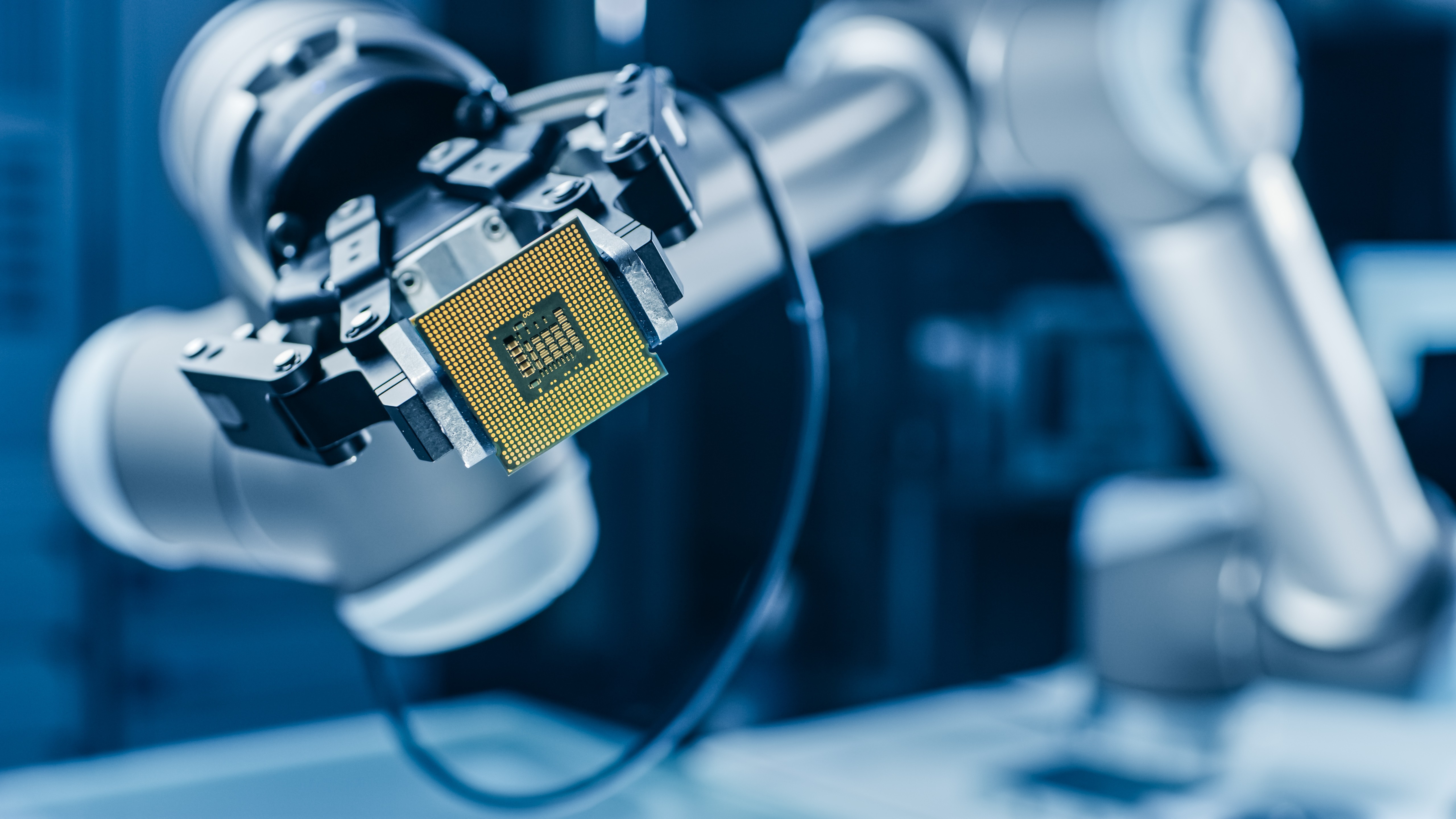 Robotic arm gripper holding a gold computer processor chip in a blue-lit industrial setting
