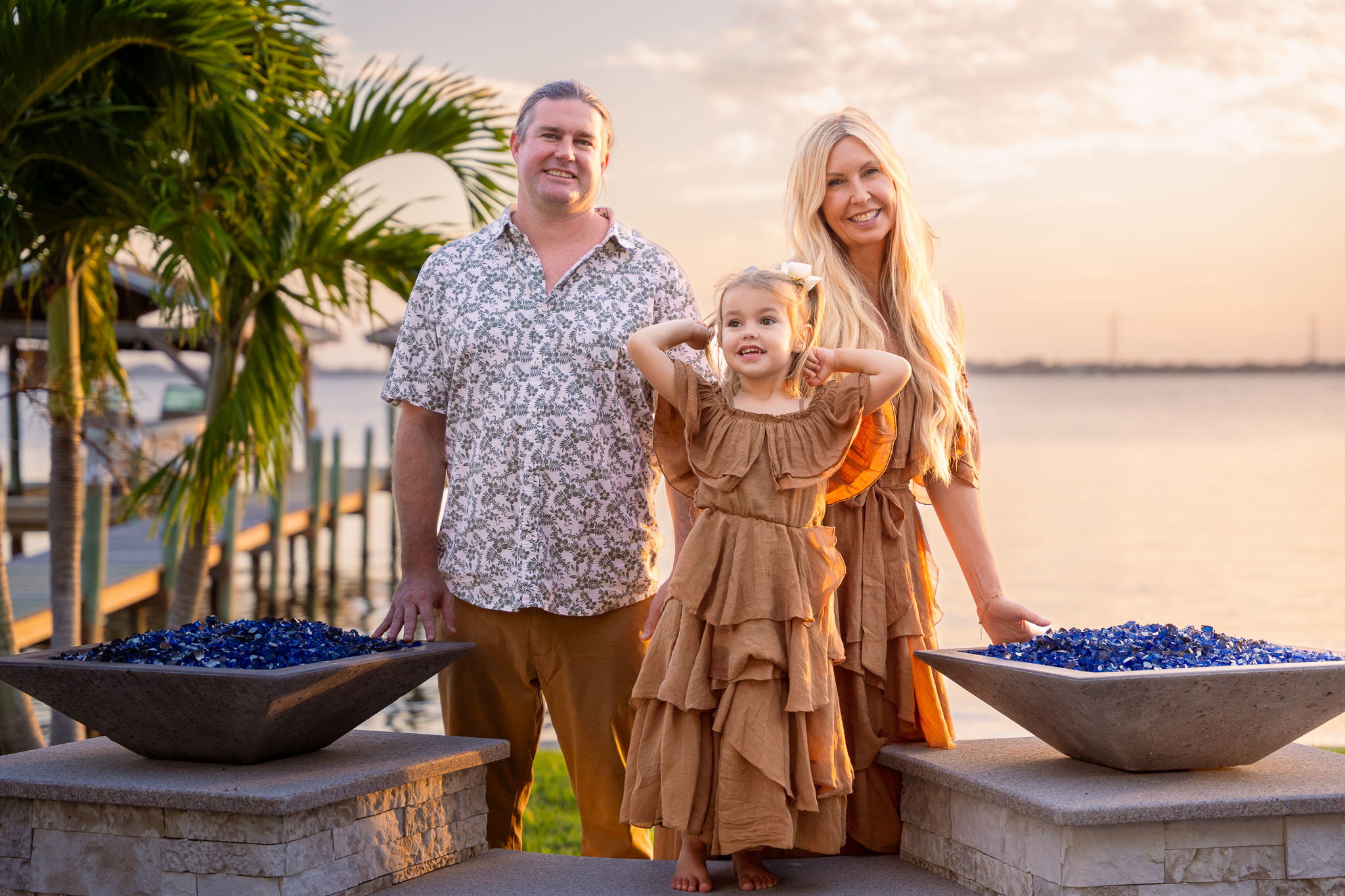  a young family standing between two pillars with palm trees to their left and a river to their right