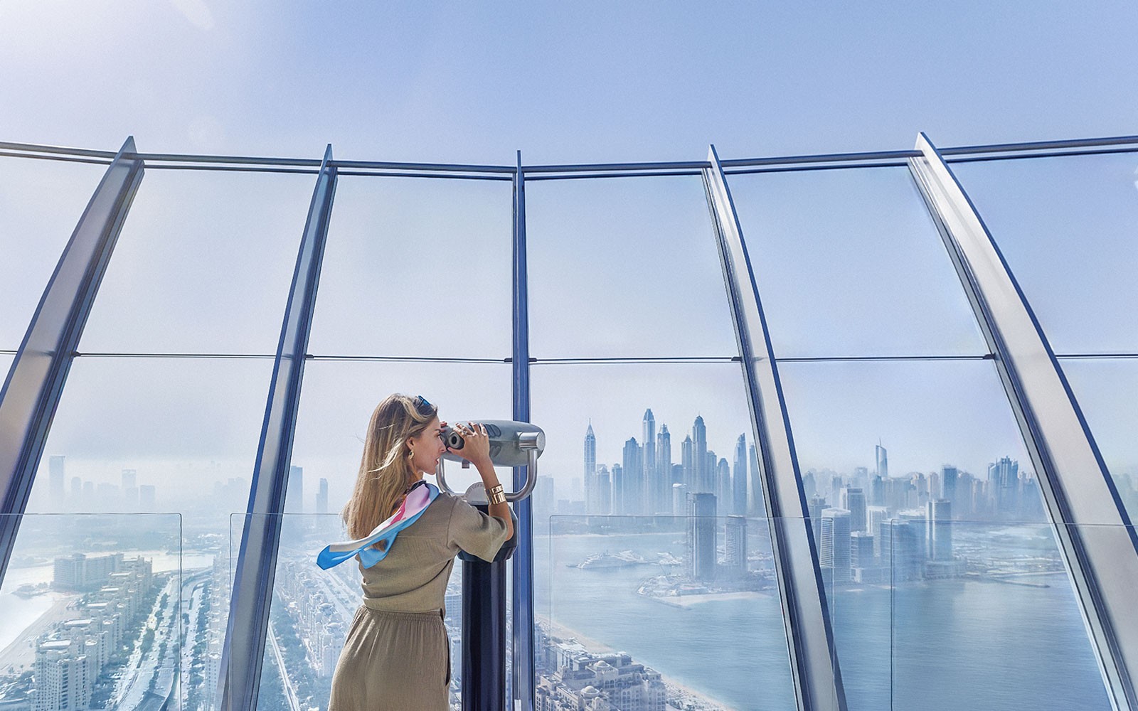 Woman using telescope to view Palm Jumeirah and Dubai skyline.