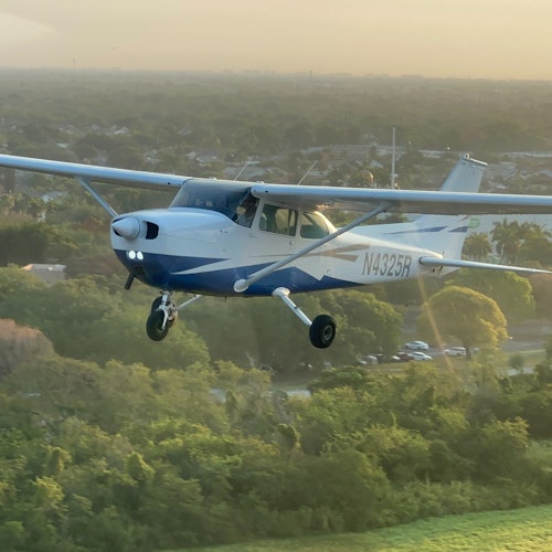 一架蓝白色小型螺旋桨飞机在日落时分飞越森林地区，可以看到飞机的注册编号N4325R。
