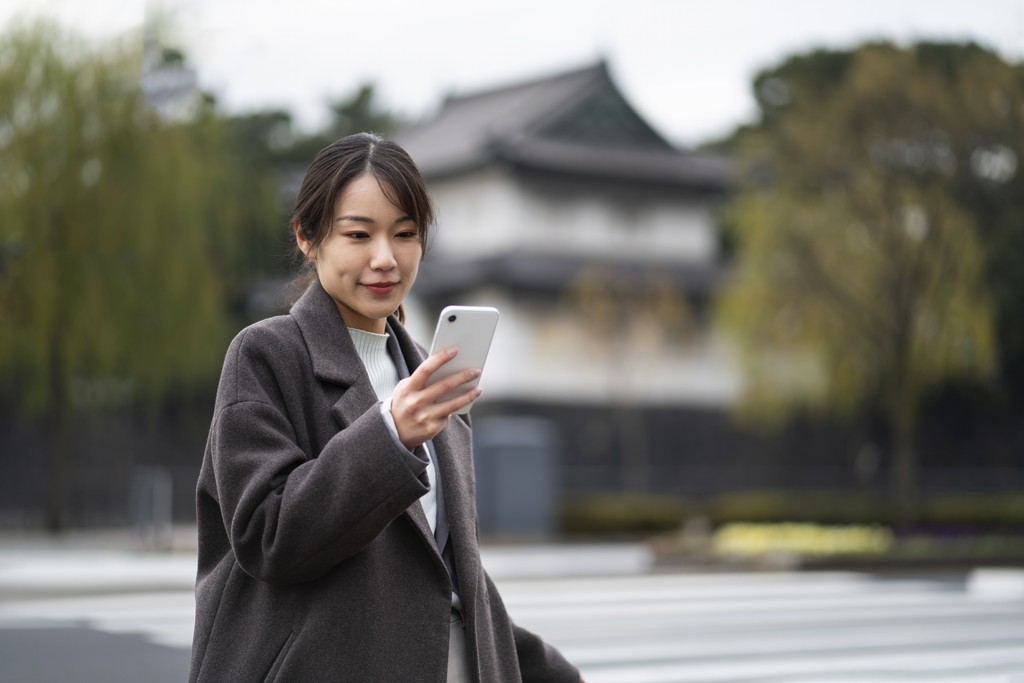 Business Japanese women walking across the street connecting their smartphone with eSIM