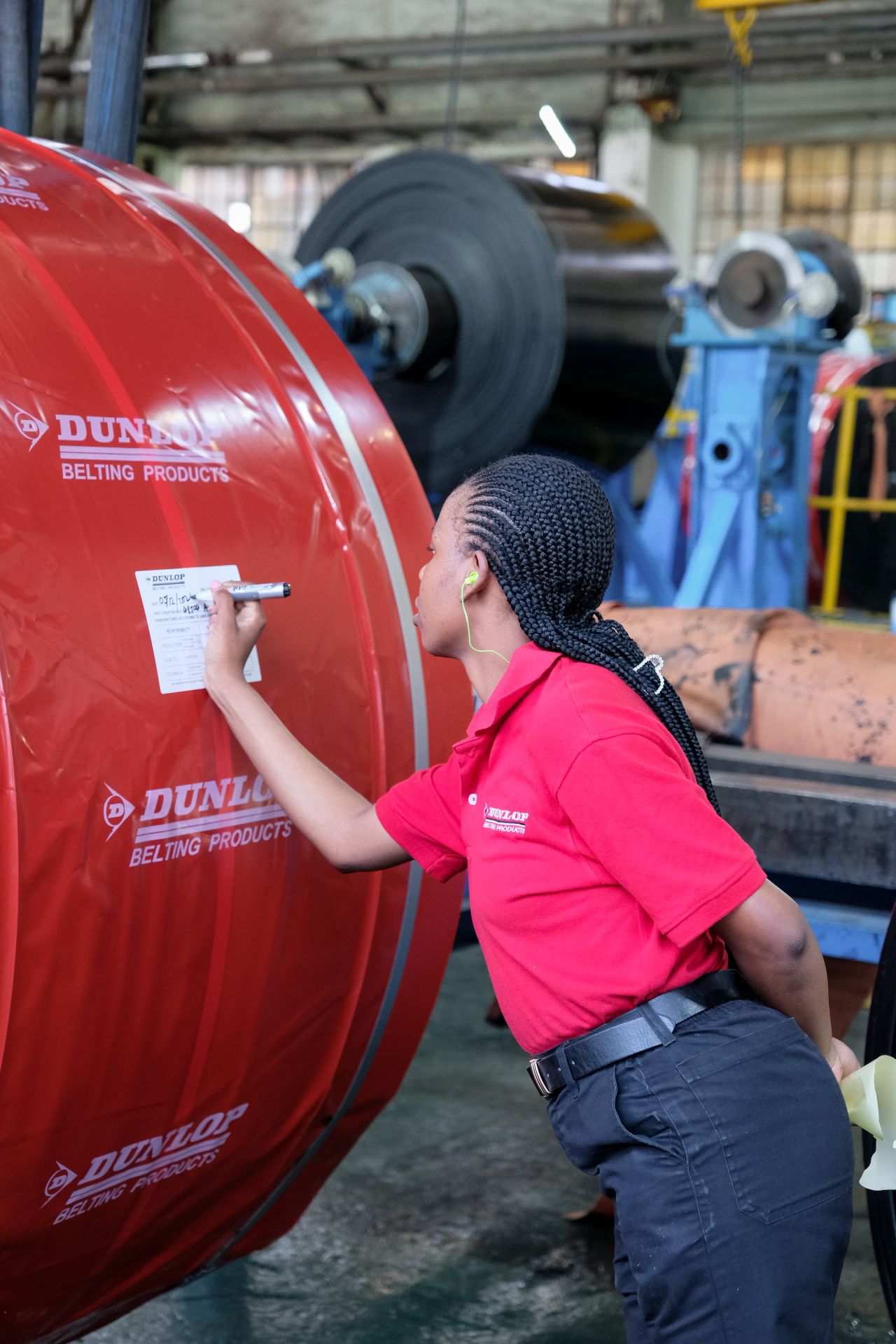 A smiling woman with her arms crossed, standing against a dark green background. She has long, dark hair.