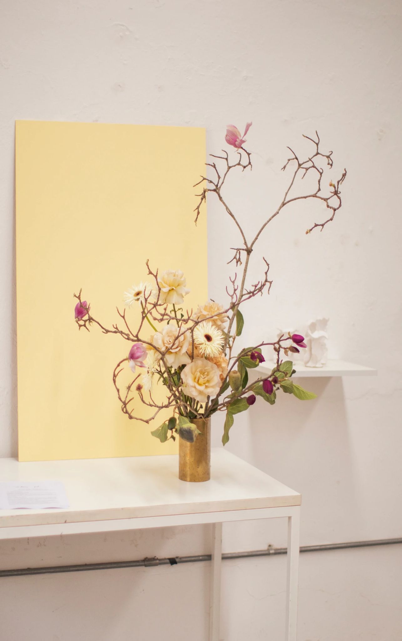 Arreglo floral con rosas blancas, magnolias rosas y ramas en jarrón dorado.