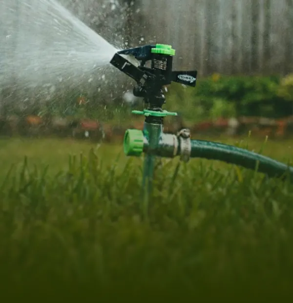 Detalle de un sistema de riego por aspersión automático en pleno funcionamiento sobre el césped verde del jardín.