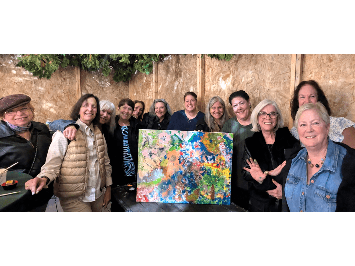Women gather around a painting at a sukkah program.