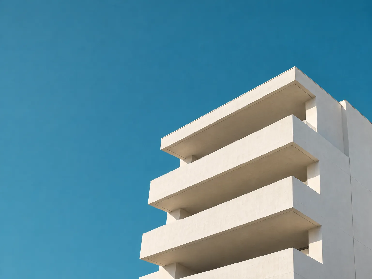 White stacked apartment balconies against a smooth teal sky