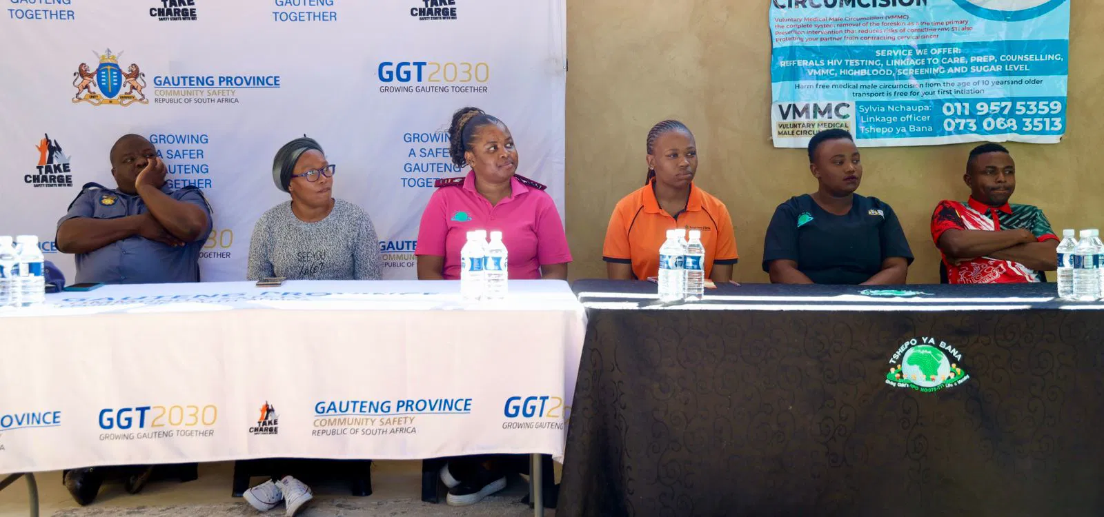 Smiling young woman with curly hair sitting at a laptop, in front of a teal wall.