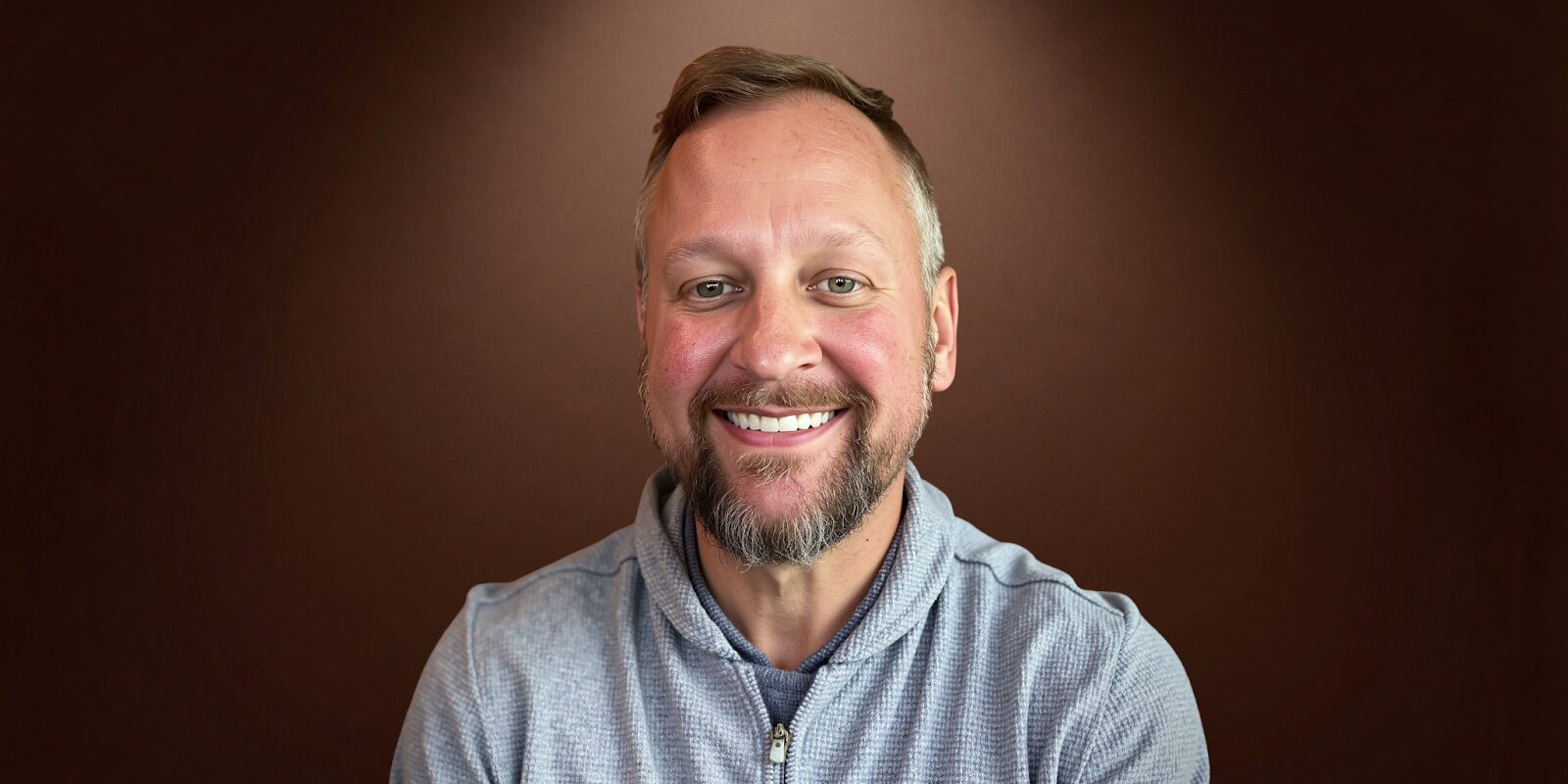 A smiling man with a beard in a blue shirt, representing Marketing Mike, founder of The Fractional CMO Team.