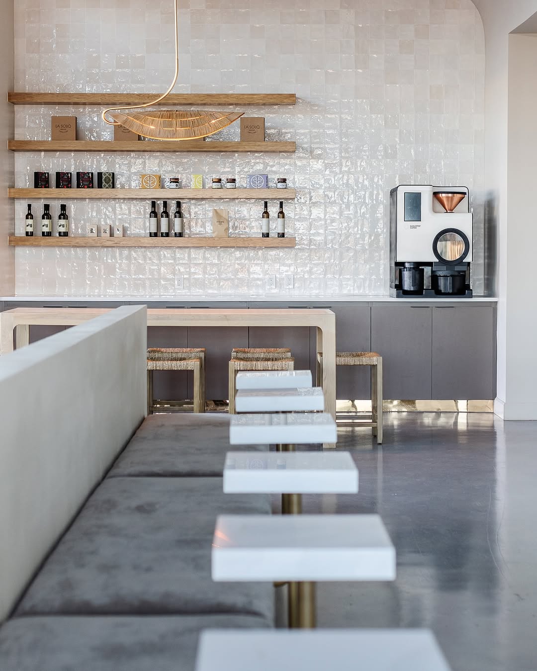 Interior of La Souq café in Dallas featuring a minimalist coffee bar with textured white tile, warm wood shelving, curated retail products, and modern seating in a calm, design-led space.