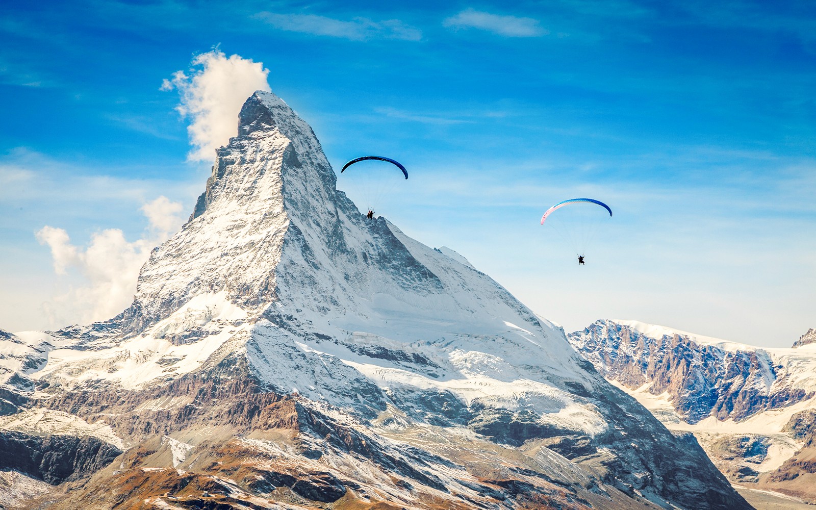 स्विट्जरलैंड में गाइड के साथ मैटरहॉर्न पर्वत के पास पैराग्लाइडर्स उड़ान भरते हुए।