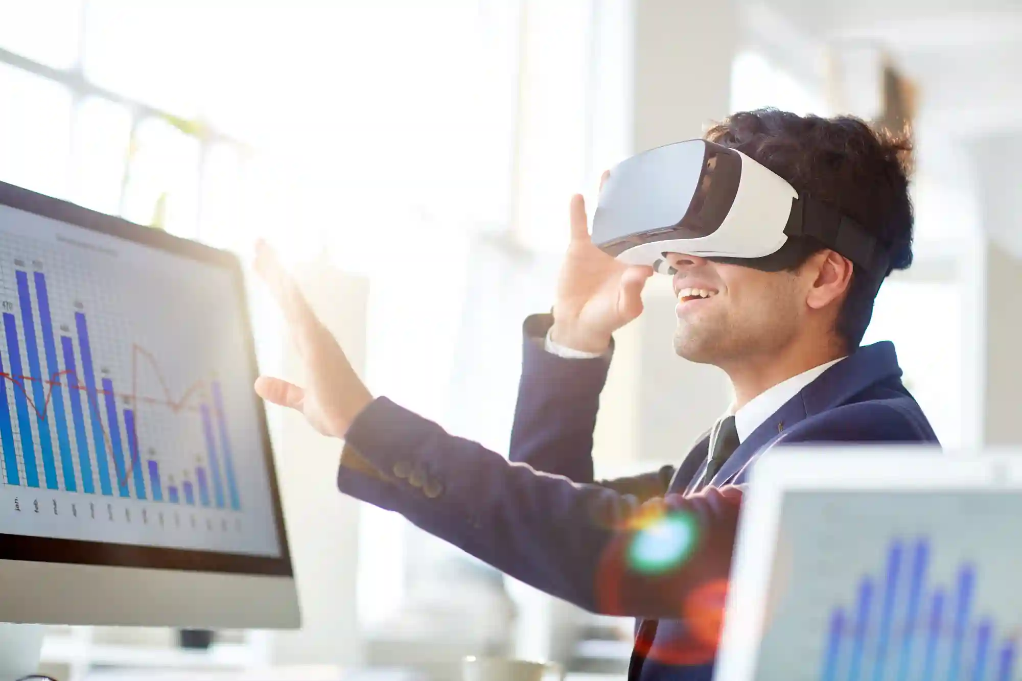 A smiling businessman wearing a VR headset while interacting with digital data charts in a bright office.