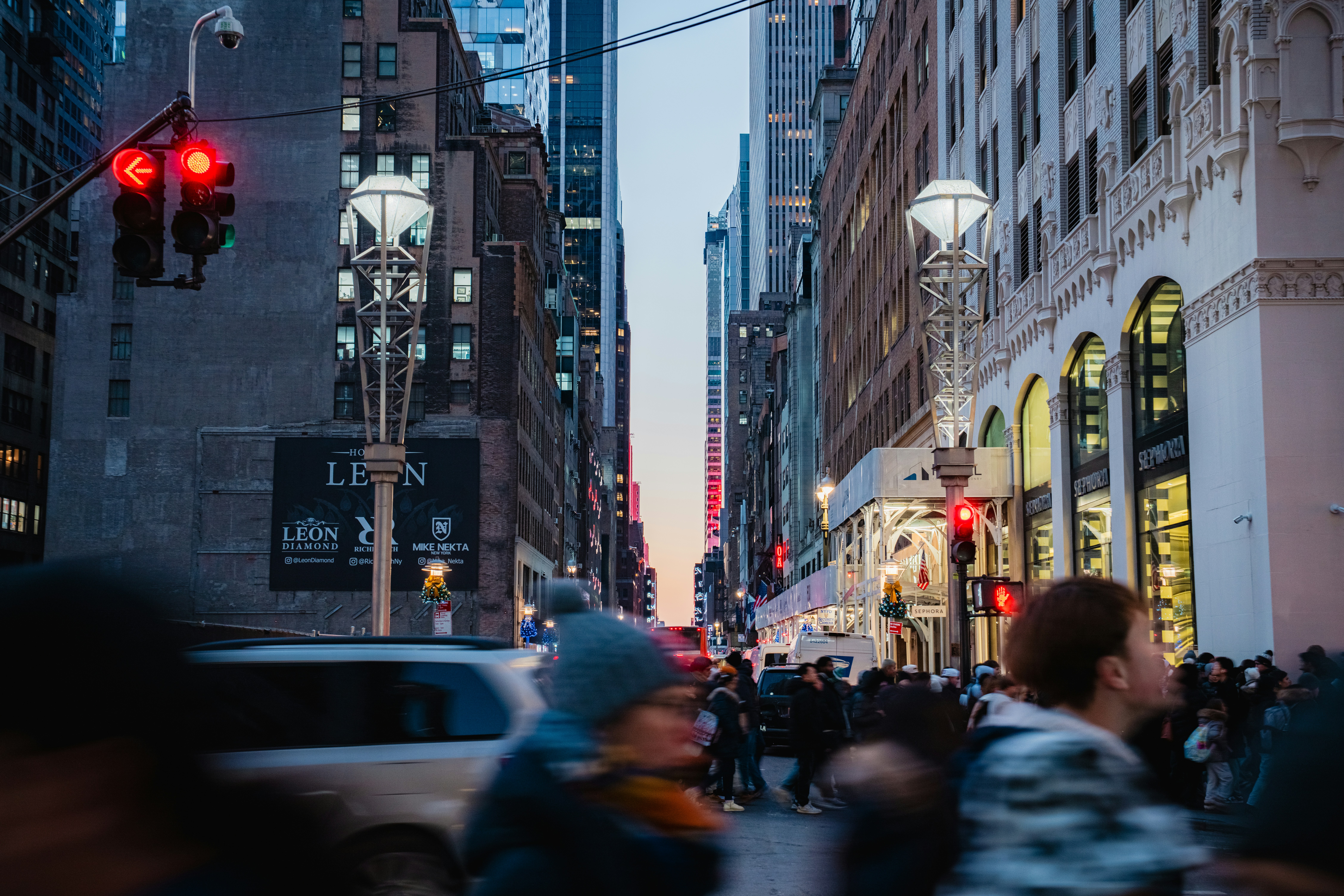 Evening urban street scene with people moving through a busy crosswalk and traffic lights