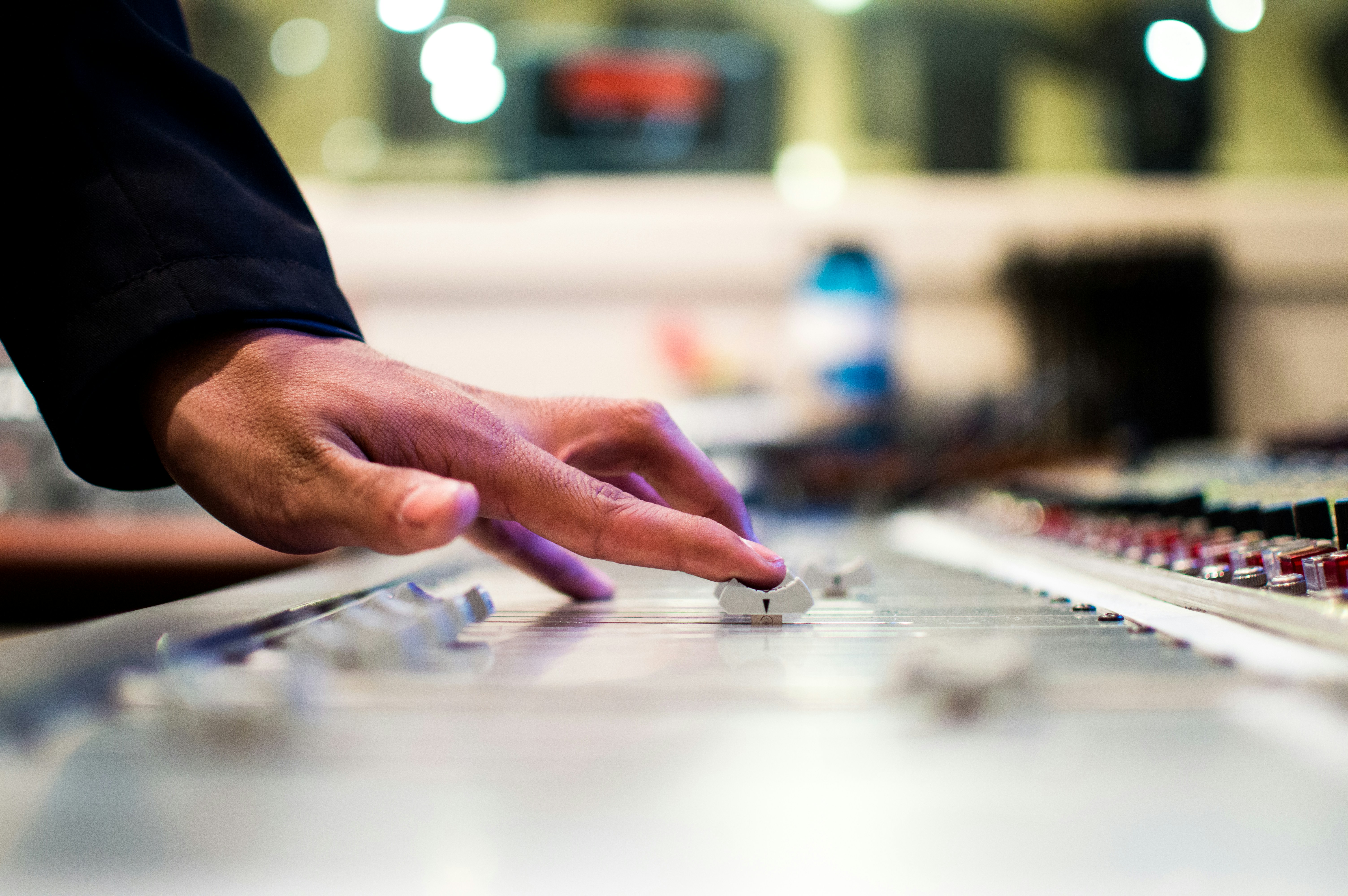 A hand adjusting a slider of a mixing board