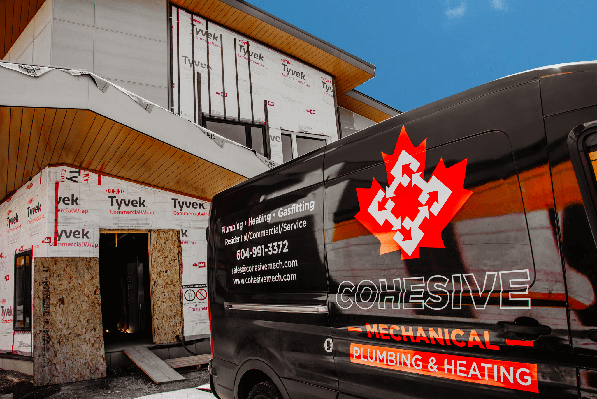A construction site featuring a partially built house and a black Cohesive Mechanical van with a logo parked nearby.