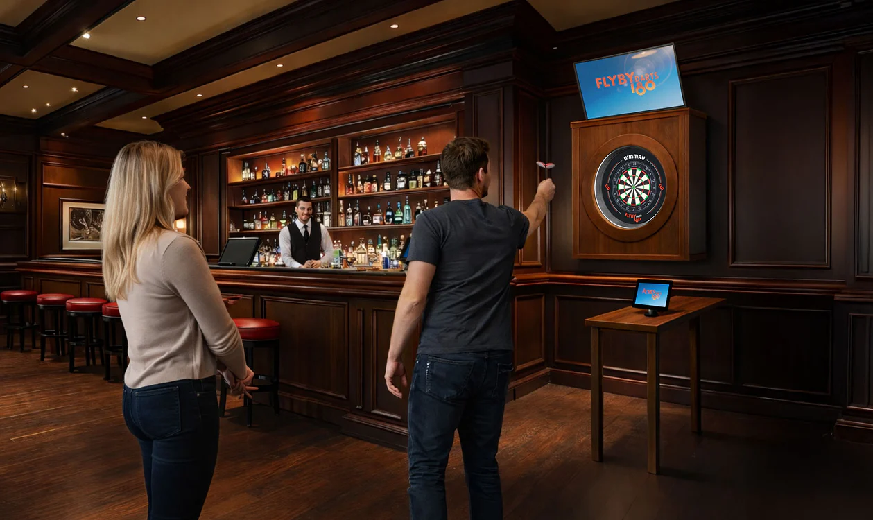 A young person with curly hair smiles at the camera while sitting in front of a laptop against a dark background.
