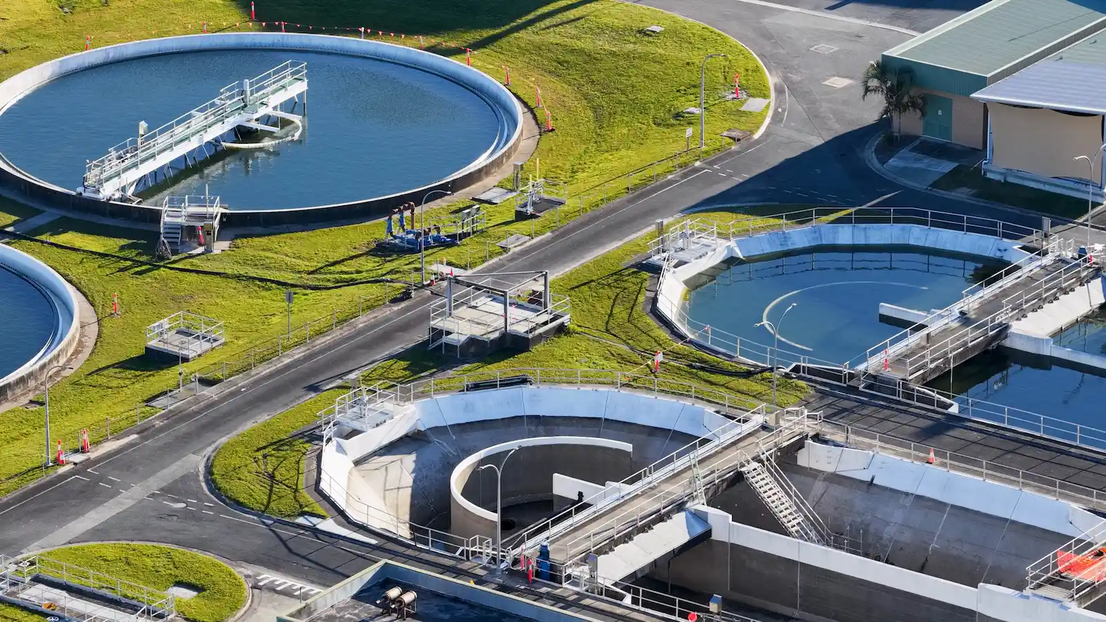 Vue aérienne d'une station de traitement des eaux : grands bassins circulaires entourés de pelouse et de passerelles.