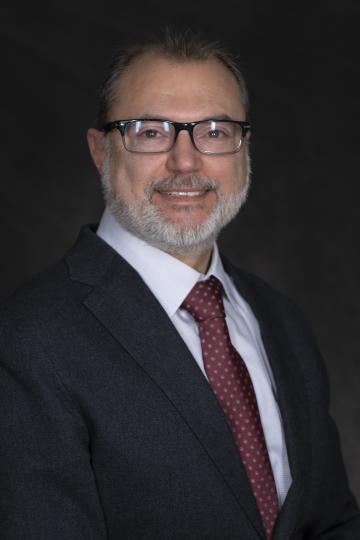 Portrait of a smiling middle-aged man with glasses, a beard, and wearing a suit and tie.