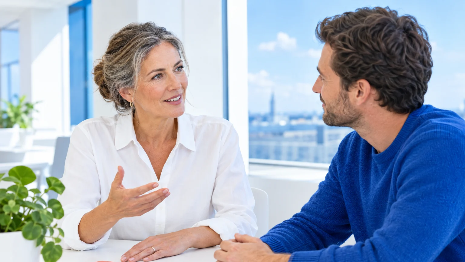 Two people talking at a bright table with a view of the city.