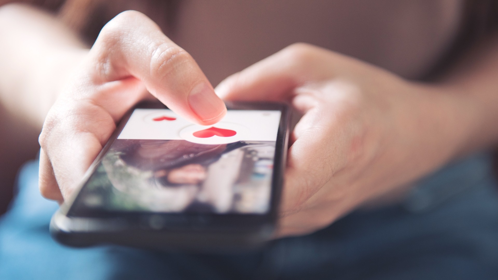 eine person bedient das handy, sie drückt auf ein herzchen und liked damit ein bild einer person