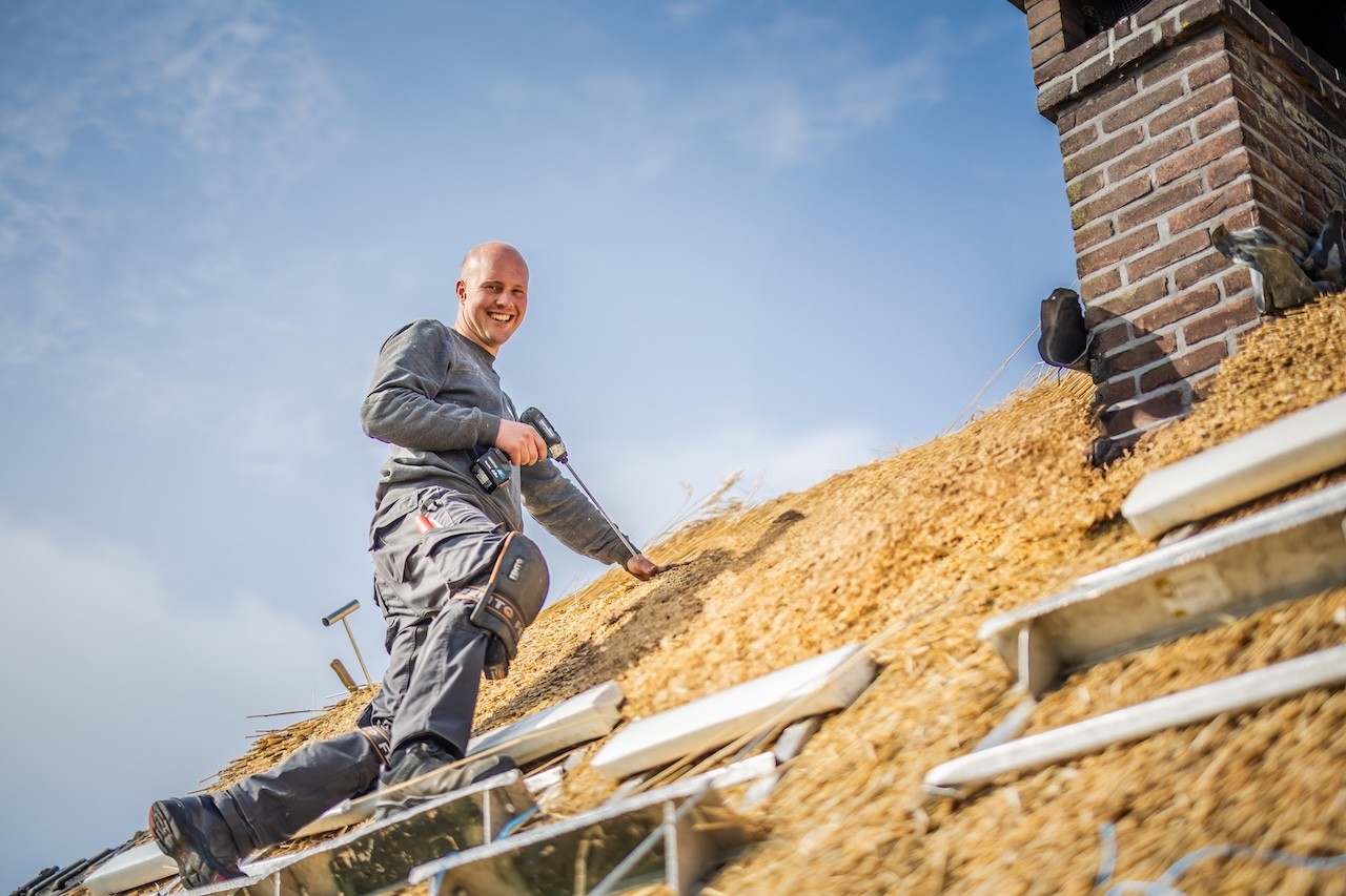 Rietdekker van Rietdekkersbedrijf van Dijk werkend aan de vervanging van dakpannen met een rieten dak