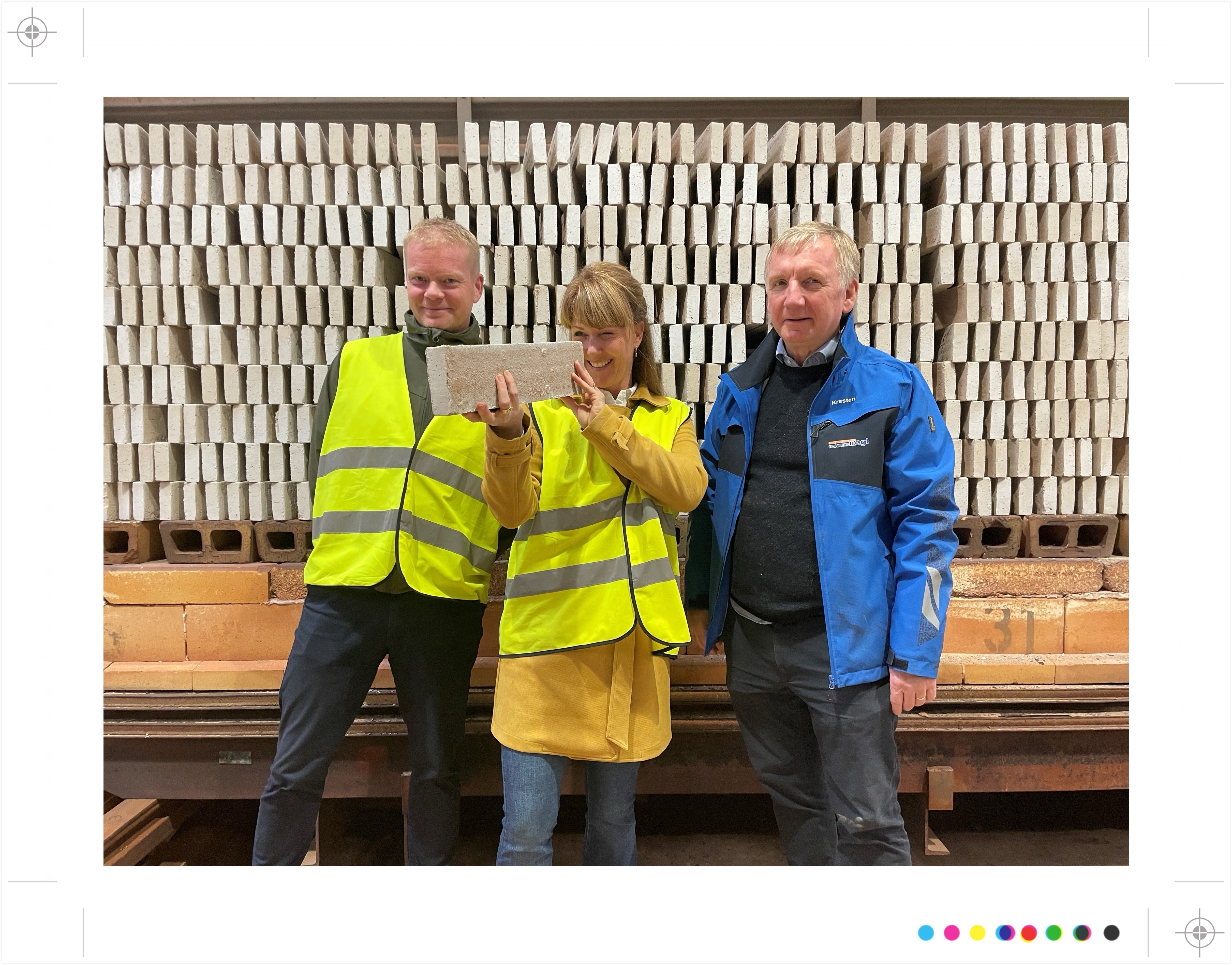 Drie mensen poseren met een baksteen in een baksteenfabriek.