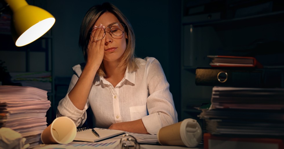 Frustrated and tired woman working under a lamp with piled up paperwork