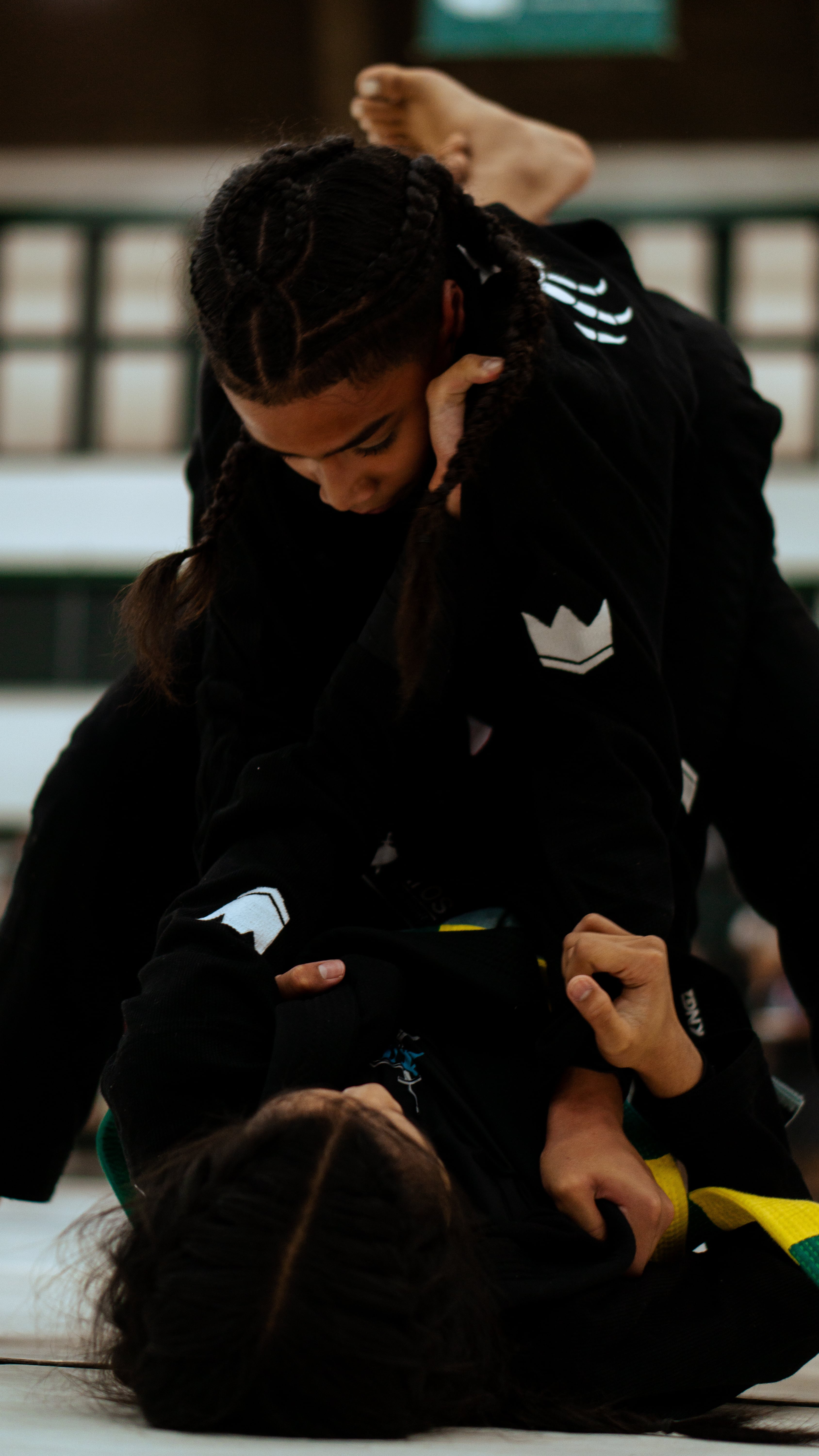 Two young children in jiu-jitsu uniforms compete on the mat, one performing a hold on the other during a Pacific Grappling Events tournament.