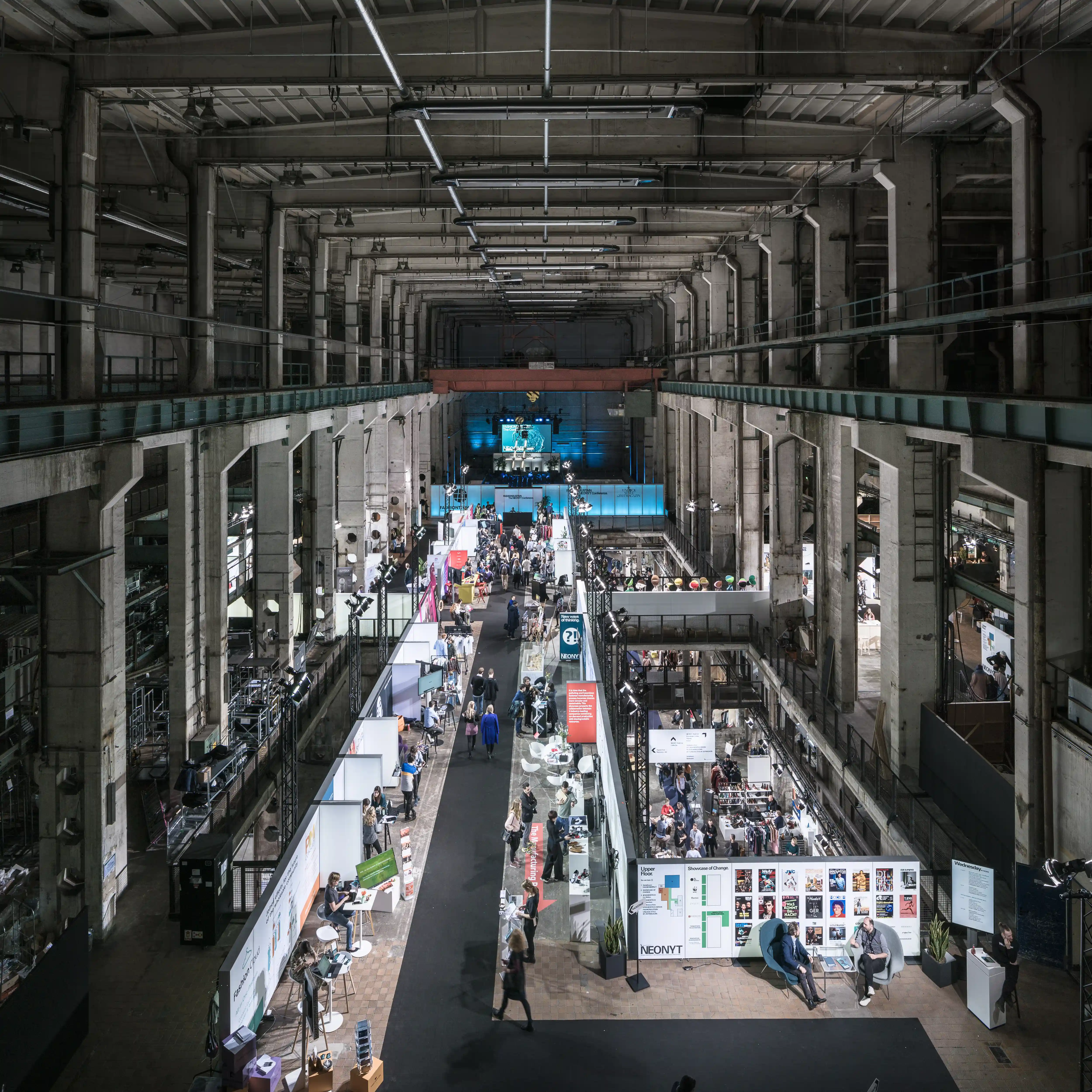 Bird's-eye view of the NEONYT trade show floor in Kraftwerk Berlin with exhibitor stands lining the central aisle between concrete pillars.