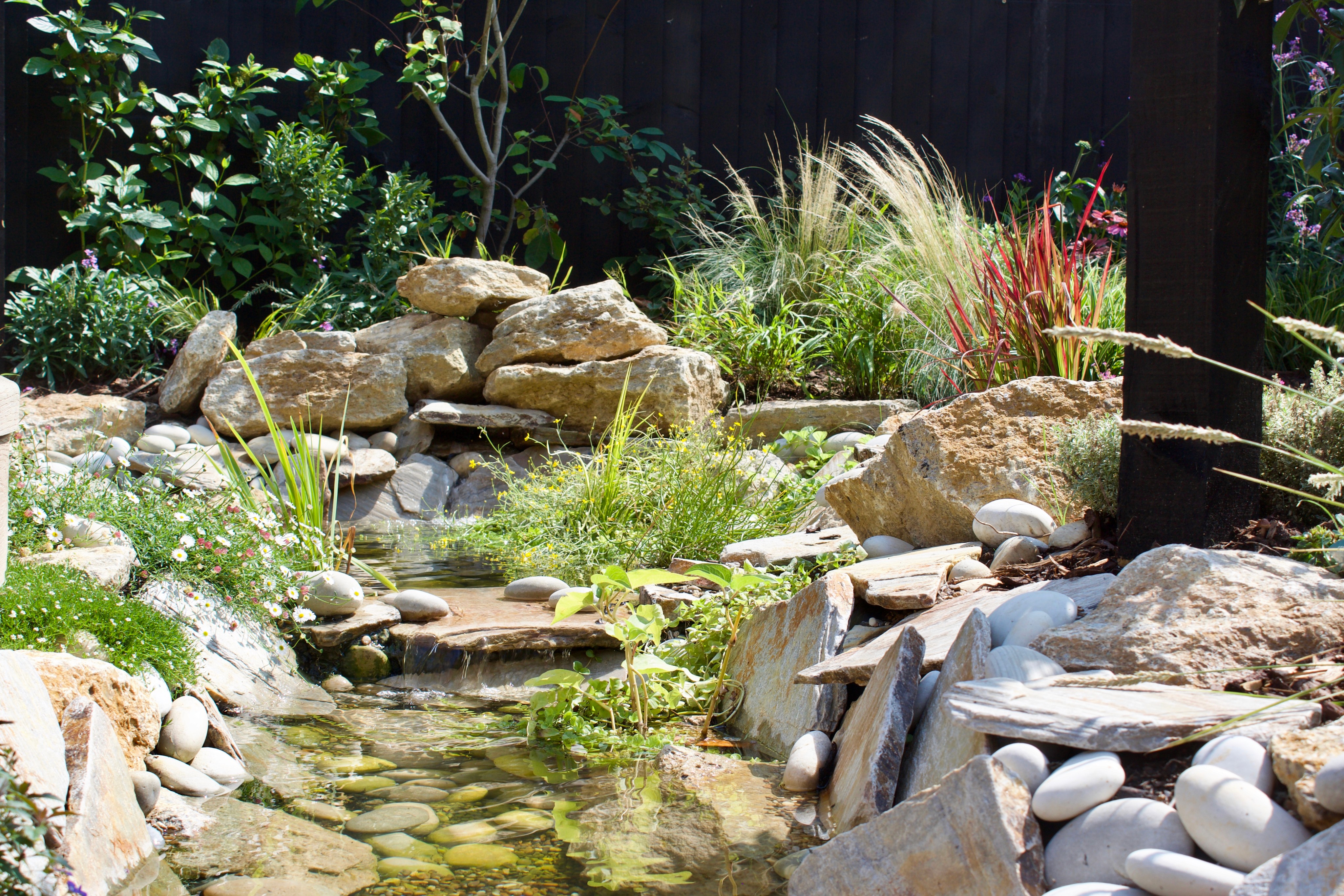 A serene garden scene featuring rocks, greenery, and a small water feature cascading down.