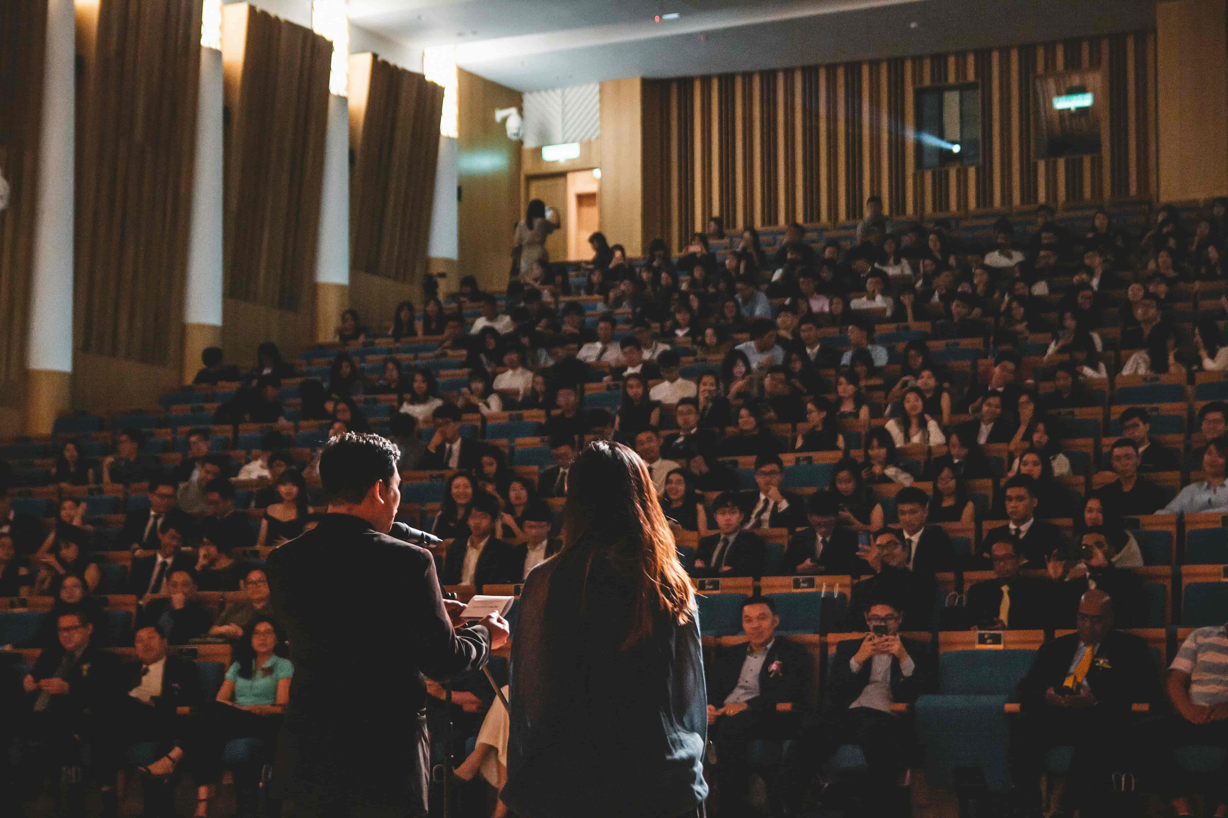 A man and woman address a large audience standing together on stage sharing ideas and insights